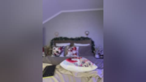 Video of a cozy, dimly lit bedroom featuring a bed adorned with red and white pillows and a festive wreath. The room's walls are pale gray, and the bed's bedding is a mix of beige and white.