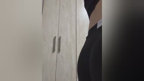 Video of a person's midsection, showing a black shirt and part of a white belt. The background features a white wooden wardrobe with vertical lines and horizontal handles.