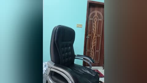 Video of a modern office chair with black upholstery and metal legs, positioned in a room with light blue walls and a wooden door with intricate carvings.