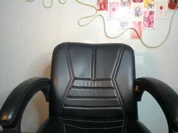 Video of a sleek, black leather office chair with geometric patterns, set against a white wall adorned with colorful post-it notes and a green cable, creating a modern, minimalist office ambiance.