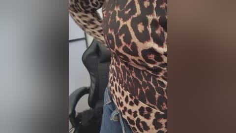 Video of a person wearing a leopard print long-sleeve shirt and blue jeans, sitting in an office chair with a black mesh backrest.