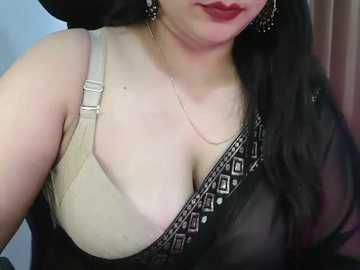 Video of a woman with fair skin, long black hair, wearing a beige bra, black sheer blouse with intricate silver embroidery, and dangling earrings. She has a hint of red lipstick.