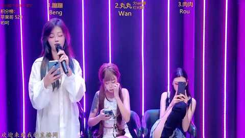 Video of three women, two standing and one seated, holding cameras, against a purple vertical LED-lit backdrop.