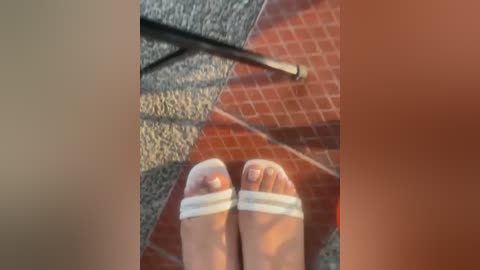 A video captures a pair of bare feet with white sandals, resting on a carpeted floor with geometric patterns. A broom handle lies beside them, indicating a domestic setting.