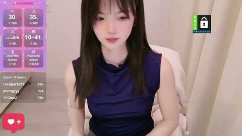 A video of a young East Asian woman with long black hair, fair skin, and a slender physique, wearing a dark blue sleeveless top, sitting in a room with soft lighting and a purple background.