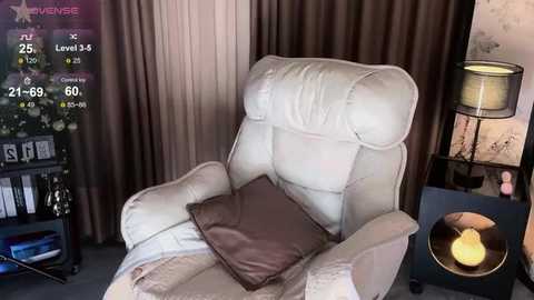 Video of a plush, cream-colored recliner with a brown pillow, situated in a cozy living room with beige curtains, a dark wooden side table, and a lit table lamp.