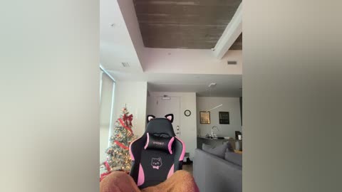 A video of a modern living room with a black gaming chair, a decorated Christmas tree, and a gray sofa, taken from a low angle.