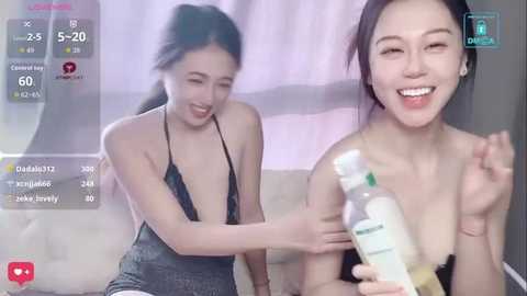 Video of two smiling Asian women in a livestream setting. One wears a black halter top, the other a strapless dress, holding a bottle.