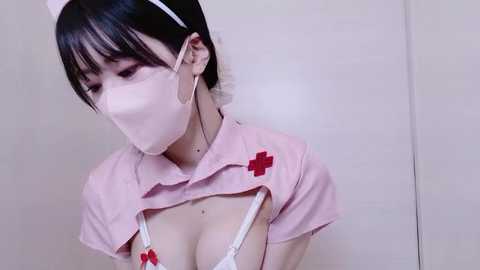 A video of an Asian woman in a revealing nurse costume, wearing a pink hat and mask, with a low-cut shirt exposing her ample cleavage.