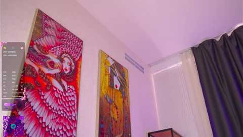 Video of a modern bedroom with three large, vibrant abstract paintings on the wall. The central painting features a woman in a flowing dress with red and yellow hues, while the left painting showcases a red bird-like figure. The room is dimly lit, with a white bed partially visible on the right.