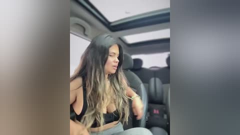 Video of a woman with long, wavy, dark hair, wearing a black top, seated in a car's backseat, eyes closed, appearing tired.