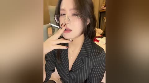Video of a young Asian woman with pale skin, black hair, and glasses, wearing a black pinstriped shirt, holding a cigarette to her lips. Background shows a cluttered room with toys and furniture.