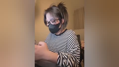 A video shows an Asian woman with glasses, black mask, and black-and-white striped shirt, seated indoors, holding a phone.