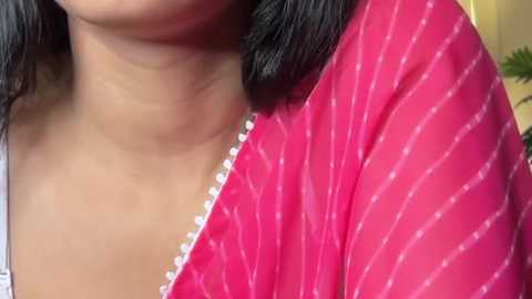 Close-up video of a woman with medium brown skin, wearing a vibrant pink saree with vertical white stripes and a gold border. Her black hair is styled in loose waves.