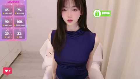A video of an East Asian woman with long black hair, fair skin, and a slender physique, wearing a sleeveless navy blue top and white jacket. Background includes a white wall, wooden floor, and a pink and purple digital screen displaying health stats.