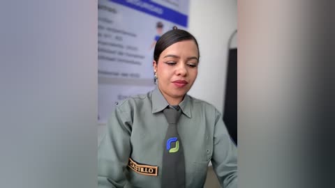 Video of a Latina woman in a green military uniform, name tag visible, with a blue tie, standing in a clean, modern room with white walls and a blue sign in the background.