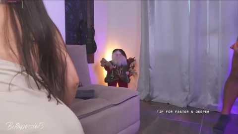 Video of a woman in a white top and another woman in a green top, both facing a glowing, animated figure in a dark room with purple and blue lighting.