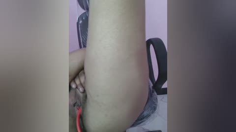 Video of a person with light brown skin, wearing a gray shirt, sitting in a black office chair. They are using a red pen to mark their inner thigh. The background is a light pink wall.