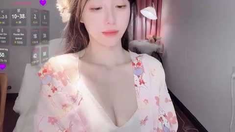 Video of a young Asian woman with fair skin, wearing a floral-patterned robe, standing in a dimly lit room with a cozy atmosphere.