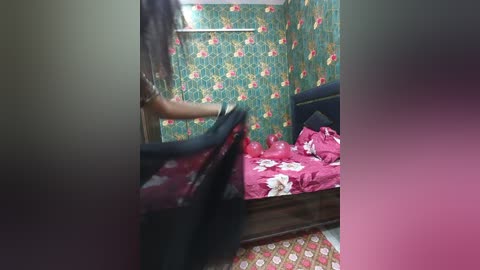 A video of a small, cluttered bedroom with floral-patterned wallpaper, a bed with red bedding, and a person in a dark shirt opening a black door.