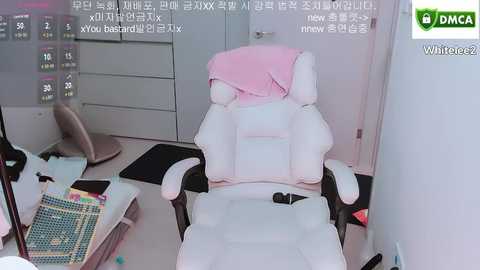 Video of a white gaming chair with a pink blanket draped over it, situated in a tidy office space with a white desk and a large calendar on the wall.