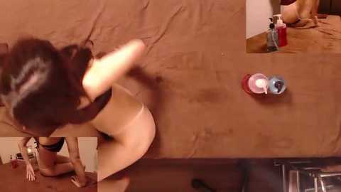 Video of a woman, possibly of Asian descent, with long dark hair, wearing a black bra and panties, leaning against a wooden table. Background includes a brown couch, a red and blue cup, and a black bottle on the table.