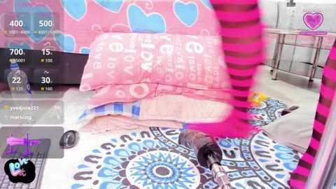 Video of a vibrant, pink-themed room with a blue mandala rug, a person wearing a heart-patterned shirt, and a microphone on the floor.