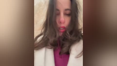 A blurred video of a woman with long, wavy brown hair, wearing a red top and white jacket, appears to be in a state of distress, eyes closed, mouth slightly open.