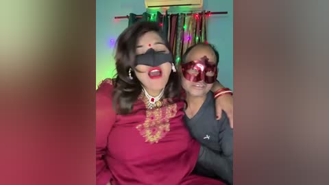 Media: Video of a woman in a burgundy sari, adorned with gold embroidery and a red bindi, and a bald man in a red mask, standing in a room with colorful lights and a fan.
