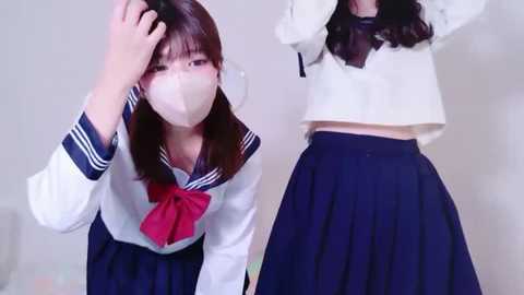 Media: Video of a young Asian woman in a school uniform, with a white mask covering her face, adjusting her hair. She has long black hair, a white blouse, navy blue skirt, and a red bow.