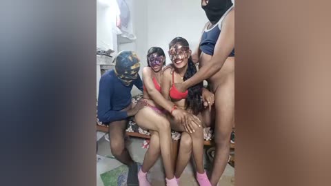 Video of a diverse group of people in a room, including a man in a blue shirt, a woman in a red bra, and others.