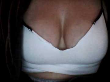 Video of a woman's cleavage in a white, low-cut sports bra. Her fair skin contrasts with the tight-fitting fabric, showcasing her ample breasts. The background is dark, making the bra's shape and color stand out.