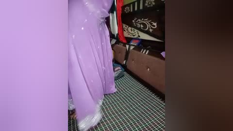 Video of a purple, shiny, inflated balloon in a room with a patterned carpet, a brown couch, and a decorative wall.