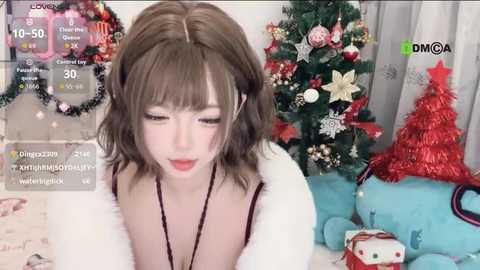 Video of a young woman with shoulder-length brown hair, wearing a white faux fur jacket, standing in a festive room with a decorated Christmas tree and plush toys.