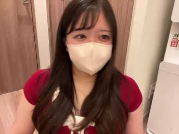 Video of a young Asian woman with long black hair, wearing a red shirt, white mask, and beige gloves, standing indoors near wooden cabinets.
