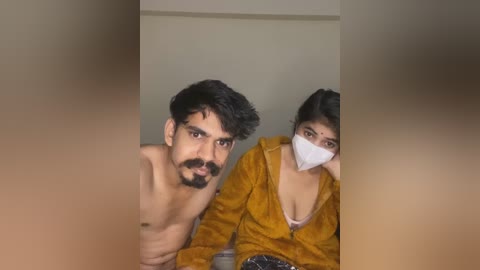 Media: A video shows a shirtless man with a beard and a woman wearing a mask, both with dark hair, sitting closely in a dimly lit room.