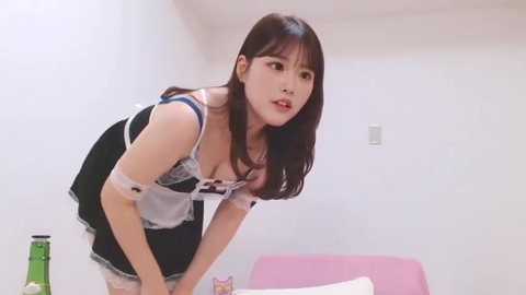 Video of an East Asian woman with straight brown hair, wearing a revealing French maid outfit, leaning over a pink bed in a white room.