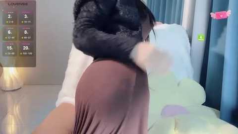 Video of a woman with dark hair and a fluffy tail, wearing a white shirt and brown skirt, lying on a bed with blue curtains.