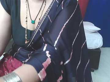 Video of a person wearing a black shirt with white stripes, red lace bra, silver bracelets, and a turquoise pendant necklace. Background shows a white bed and blue wall.