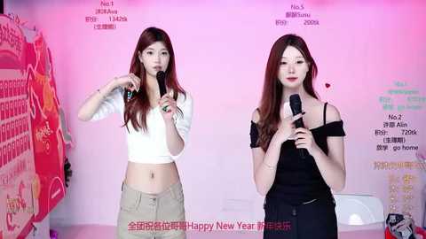 Video of two Asian women, one in a white crop top and beige pants, the other in a black off-shoulder top, singing into microphones against a pink wall with Chinese text.