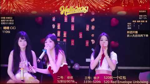 Video of four Asian women on stage, singing into microphones, wearing colorful, festive outfits. Background features a dimly lit, red and gold festive setting.