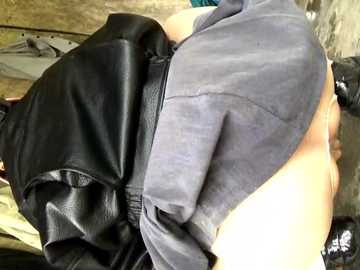 Video of a woman's bare backside, partially covered by a black leather jacket and gray shirt, sitting on a wooden floor.