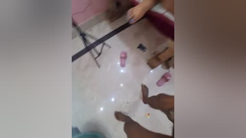 Video of a white woman with long red hair, wearing a pink dress, standing in a bathroom, holding a pink shoe, surrounded by dark-skinned hands and feet.