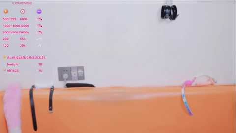 A video of a bathtub with a pink towel and black leather belt hanging over the edge, against a white tiled wall.