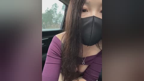Video of an Asian woman with long, dark hair, wearing a black face mask and a purple off-shoulder top, sitting in a car, blurred background.