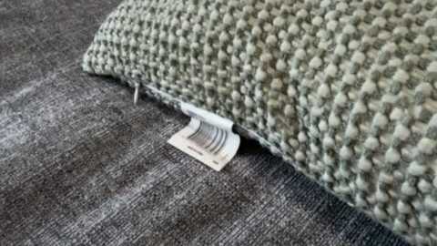 A video of a torn, textured, green and gray woven rug with a visible label and a close-up view of the damaged edge.