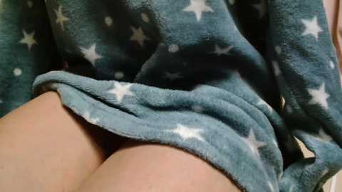Video of a person wearing a blue fleece robe with white star patterns, partially lifted to reveal bare thighs. The focus is on the lower body, with the robe's soft texture and skin tones visible.