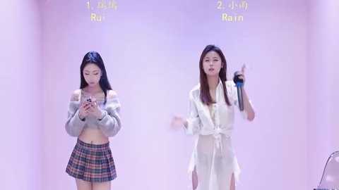 Video of two young Asian women in a bright, minimalist room. One wears a plaid skirt, the other a white dress. Text reads \"1st place Ruin.\
