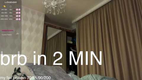 Video of a cozy bedroom with beige curtains, a chandelier, and a mirror reflecting part of the room. Text overlays read \"in 2 MIN\" and \"my fav outfit zara 29/2/2000.\