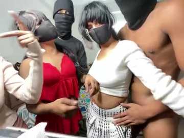 Video of a group of three women with black masks and white shirts, holding hands, in a room with colorful patterns on the walls.